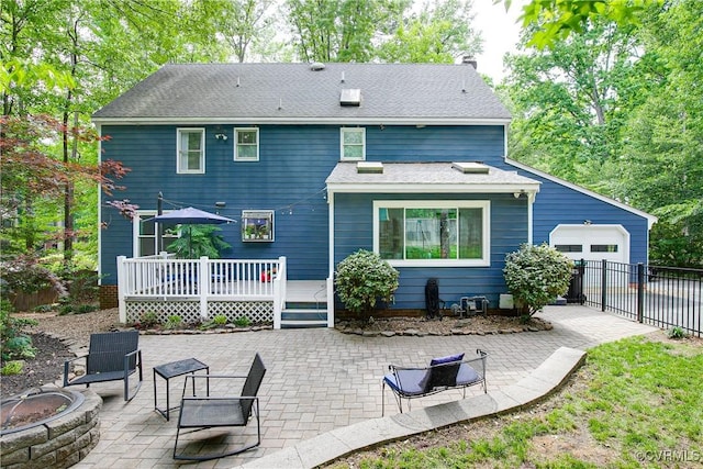 back of house with an attached garage, a fire pit, fence, a deck, and a patio area