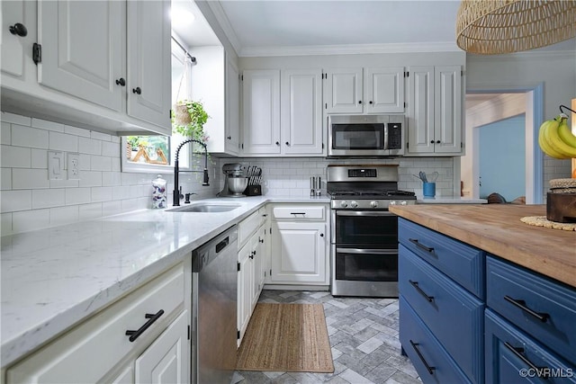 kitchen with a sink, blue cabinets, crown molding, white cabinets, and appliances with stainless steel finishes