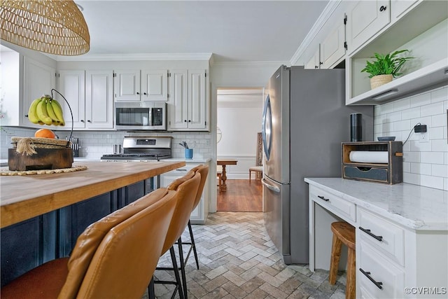 kitchen with brick floor, crown molding, decorative backsplash, white cabinets, and appliances with stainless steel finishes