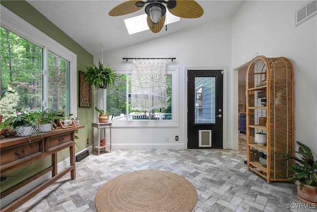 interior space featuring ceiling fan, visible vents, baseboards, and vaulted ceiling with skylight