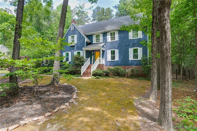 colonial house featuring fence, a front lawn, and a chimney