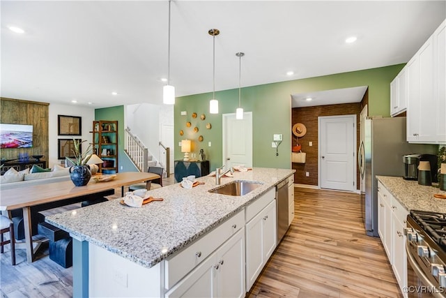 kitchen featuring appliances with stainless steel finishes, a sink, open floor plan, white cabinets, and light wood-type flooring