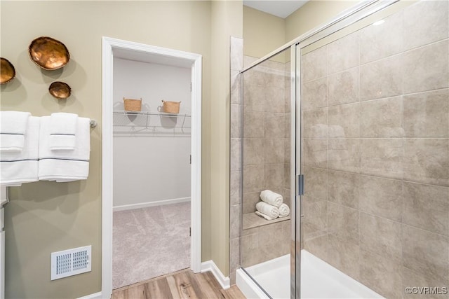full bath featuring wood finished floors, a stall shower, a walk in closet, visible vents, and baseboards