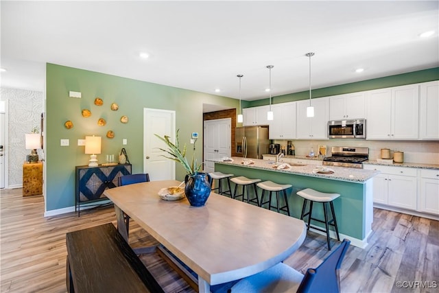 kitchen with light wood-type flooring, an island with sink, white cabinets, and appliances with stainless steel finishes