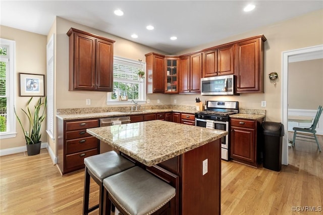 kitchen with appliances with stainless steel finishes, light wood-style floors, recessed lighting, a breakfast bar area, and glass insert cabinets