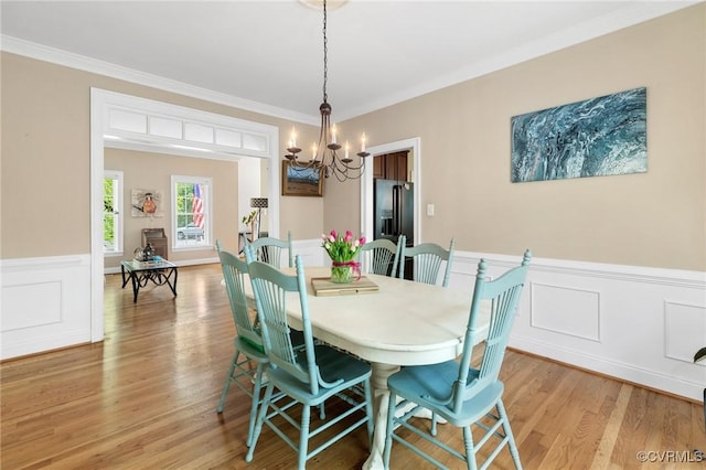 dining room featuring a chandelier, ornamental molding, a wainscoted wall, light wood-type flooring, and a decorative wall