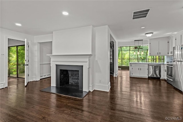 unfurnished living room featuring a baseboard heating unit, healthy amount of natural light, dark wood finished floors, a fireplace with raised hearth, and recessed lighting