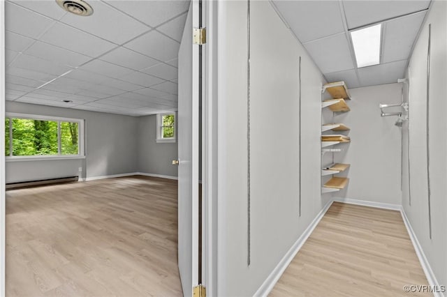 hall with baseboard heating, a drop ceiling, wood finished floors, and baseboards