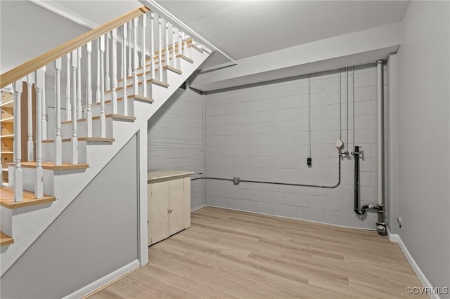 below grade area with stairs, light wood-style floors, and baseboards