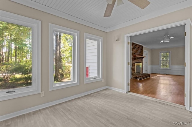 spare room with a ceiling fan, wood finished floors, a brick fireplace, and baseboards
