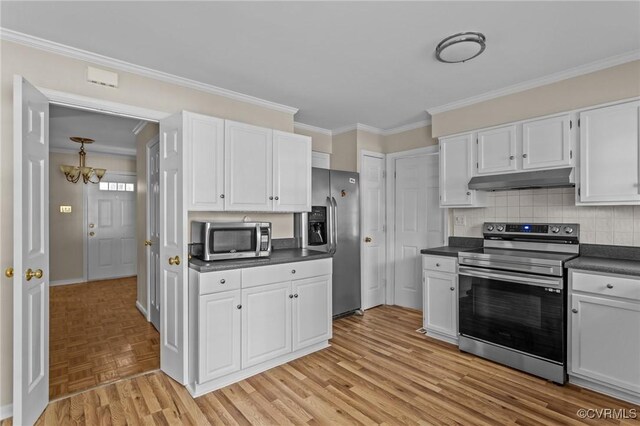 kitchen featuring appliances with stainless steel finishes, under cabinet range hood, dark countertops, a chandelier, and ornamental molding