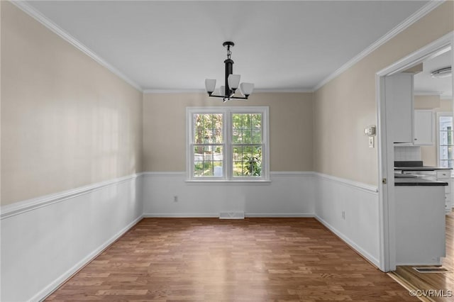 unfurnished dining area with wood finished floors, a chandelier, crown molding, and baseboards