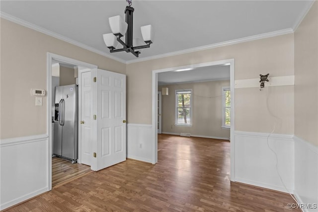 empty room with a chandelier, wood finished floors, crown molding, and baseboards