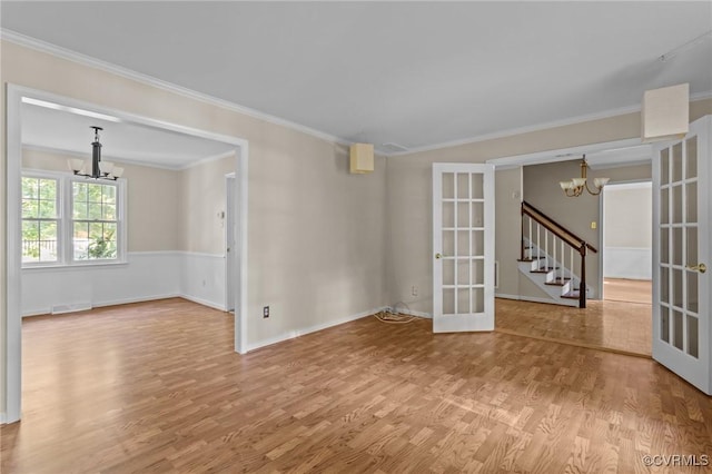 spare room featuring a chandelier, french doors, wood finished floors, ornamental molding, and stairs