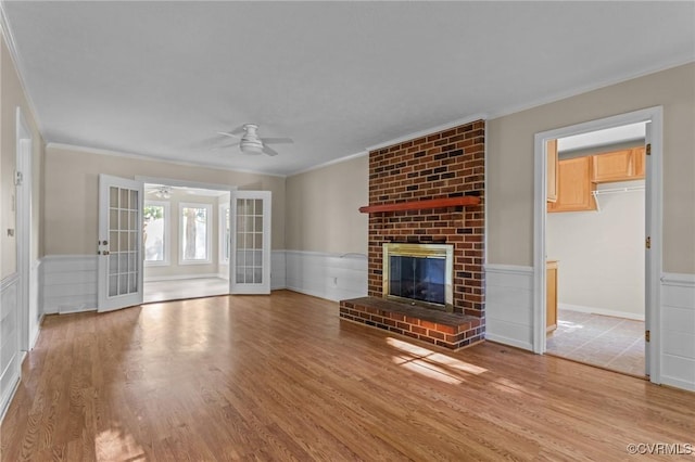 unfurnished living room with crown molding, a ceiling fan, wood finished floors, french doors, and a fireplace