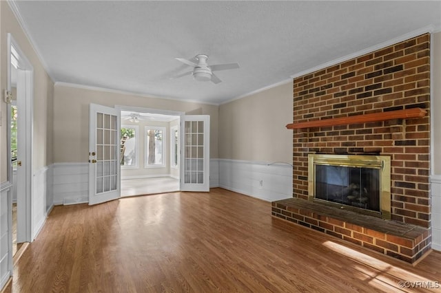 unfurnished living room featuring french doors, ceiling fan, wainscoting, wood finished floors, and ornamental molding