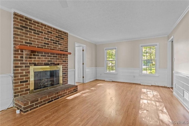 unfurnished living room with wainscoting, wood finished floors, crown molding, and a fireplace