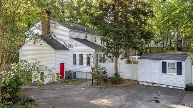 back of house featuring central air condition unit, fence, a shed, an outbuilding, and a chimney