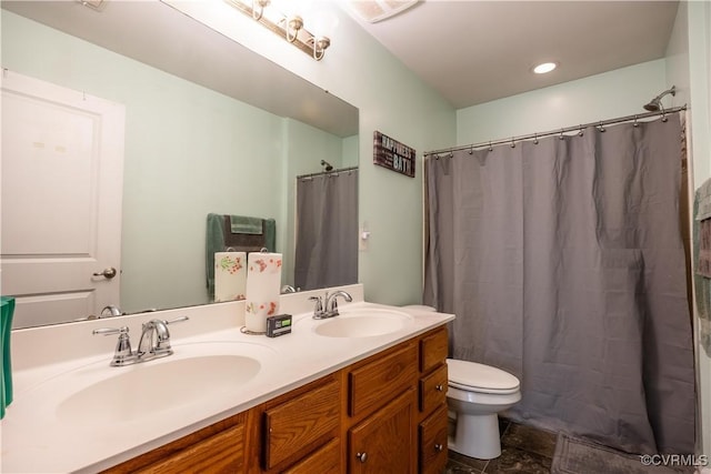 bathroom featuring toilet, double vanity, stone finish flooring, and recessed lighting