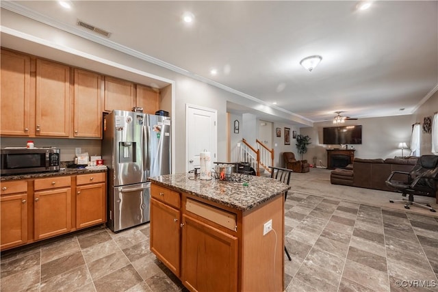 kitchen with appliances with stainless steel finishes, a center island, dark stone countertops, ornamental molding, and ceiling fan