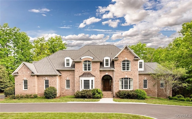 french provincial home with brick siding and a front yard