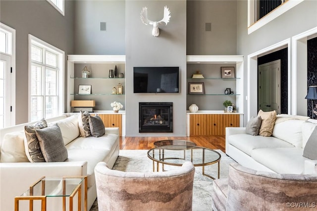 living area featuring visible vents, wood finished floors, a towering ceiling, and a glass covered fireplace