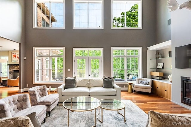 living room featuring a high ceiling, wood finished floors, a stone fireplace, and a healthy amount of sunlight