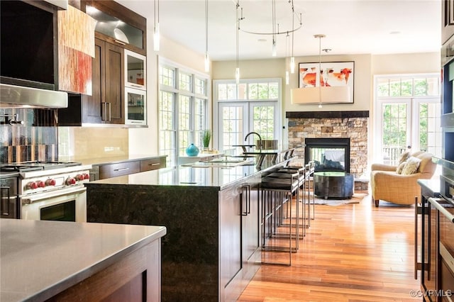 kitchen with high end stove, a fireplace, pendant lighting, light wood-type flooring, and decorative backsplash