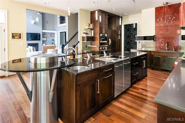 kitchen with a large island with sink, light wood-style floors, decorative backsplash, and a sink