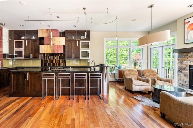 kitchen with glass insert cabinets, dark brown cabinets, a breakfast bar, light wood finished floors, and backsplash