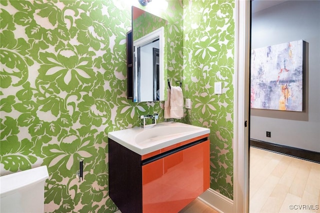 bathroom featuring vanity, baseboards, wallpapered walls, and wood finished floors