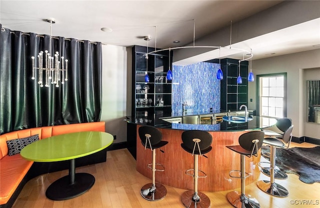 bar with baseboards, a sink, wet bar, dishwashing machine, and wood finished floors