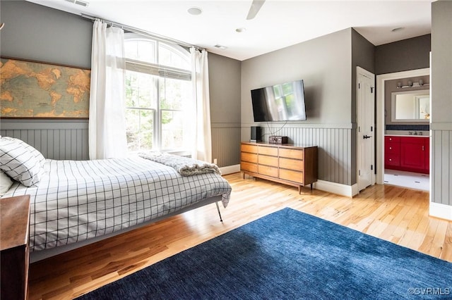 bedroom featuring a wainscoted wall, ensuite bathroom, and wood finished floors
