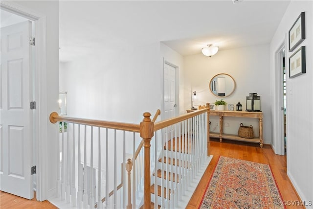 corridor with an upstairs landing, wood finished floors, and baseboards