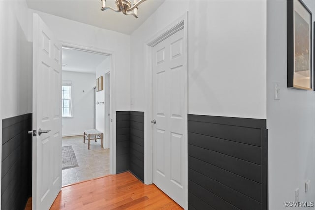 corridor with wainscoting, a chandelier, and light wood finished floors