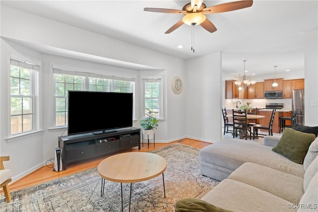 living room featuring light wood-type flooring, a ceiling fan, recessed lighting, a chandelier, and baseboards
