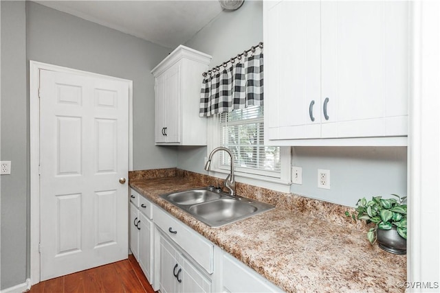 kitchen with a sink, white cabinets, dark wood-style floors, and light countertops