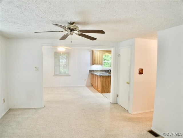 spare room with light carpet, a textured ceiling, baseboards, and a ceiling fan