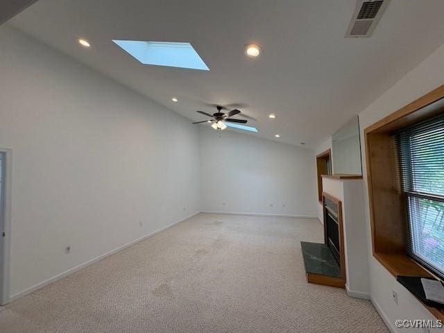 unfurnished living room featuring vaulted ceiling, a skylight, light carpet, a fireplace with raised hearth, and recessed lighting