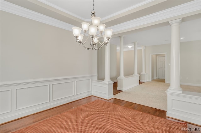 unfurnished dining area featuring wood finished floors, wainscoting, ornamental molding, and a chandelier