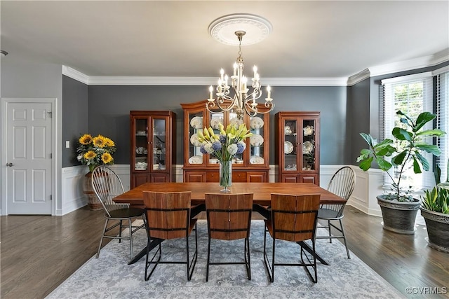dining space with a chandelier, dark wood finished floors, ornamental molding, wainscoting, and a decorative wall