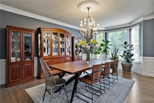 dining area with a chandelier, ornamental molding, a wainscoted wall, and dark wood finished floors