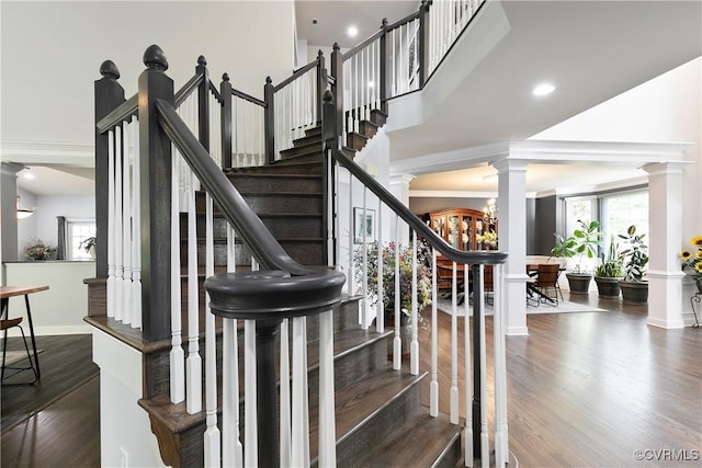stairway featuring wood finished floors, baseboards, decorative columns, a towering ceiling, and ornamental molding