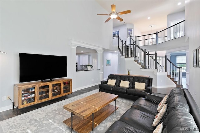 living area with a towering ceiling, a ceiling fan, stairs, wood finished floors, and baseboards