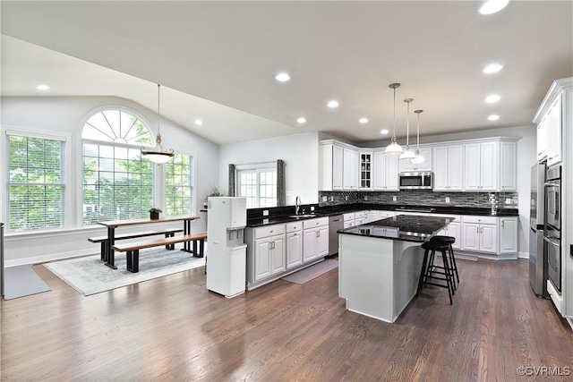 kitchen with appliances with stainless steel finishes, dark countertops, white cabinets, backsplash, and a kitchen island