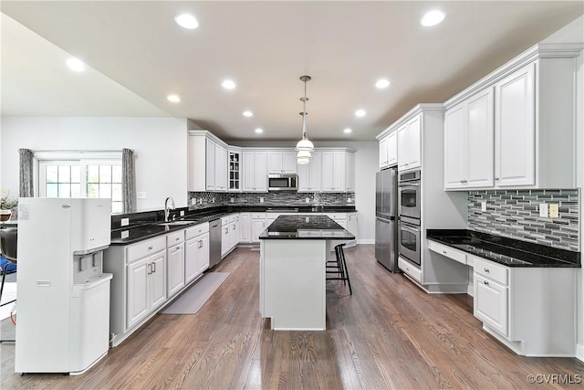 kitchen featuring stainless steel appliances, a sink, a kitchen island, a kitchen breakfast bar, and white cabinetry