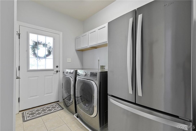 clothes washing area with washer and clothes dryer, light tile patterned floors, and cabinet space