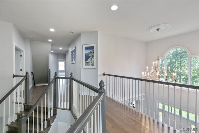 corridor with wood finished floors, a chandelier, plenty of natural light, recessed lighting, and an upstairs landing