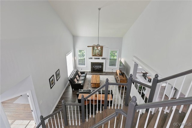 living room featuring high vaulted ceiling, ceiling fan, a fireplace with flush hearth, wood finished floors, and baseboards
