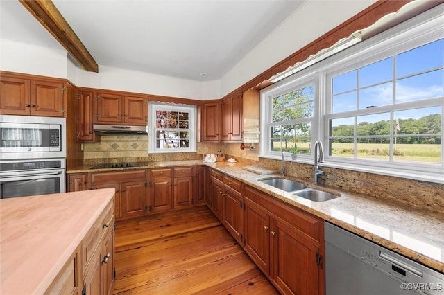 kitchen featuring stainless steel appliances, under cabinet range hood, a sink, light wood-style floors, and healthy amount of natural light